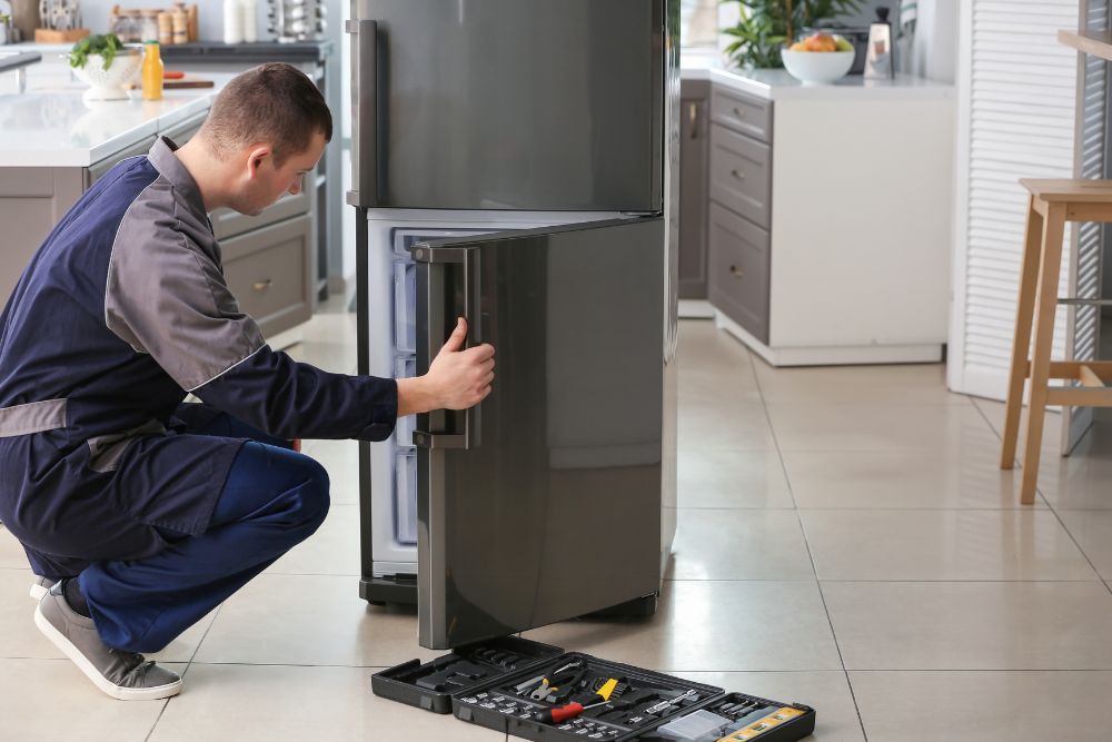 A man fixes a refrigerator in a kitchen, highlighting small appliance repair services available in Springfield, IL.